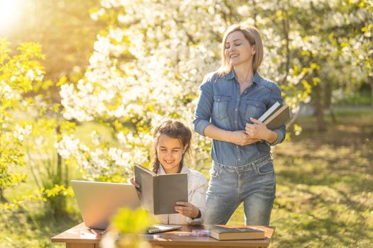 Mother helping her little daughter to use laptop computer. Child studying at home doing her homework or having online lesson. Homeschooling concept