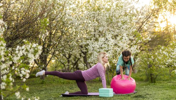 a young mother and daughter perform yoga exercises in the park on a gym mat. healthy lifestyle