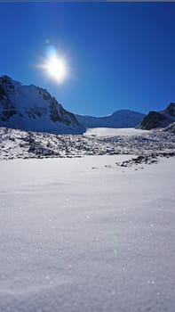 High rocks covered with snow. The Tuyuk Su Glacier. The view from the drone to the tops of the peaks. Completely surrounded by winter mountains. blue clear sky and bright sun. Shadows from mountains