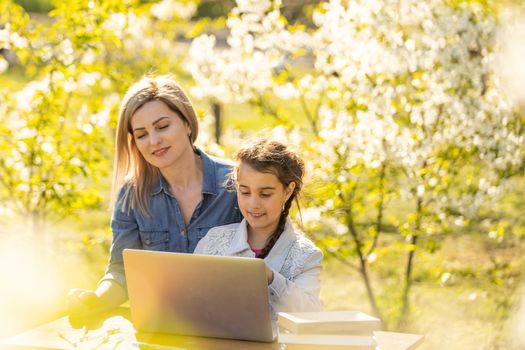 Mother helping her little daughter to use laptop computer. Child studying at home doing her homework or having online lesson. Homeschooling concept