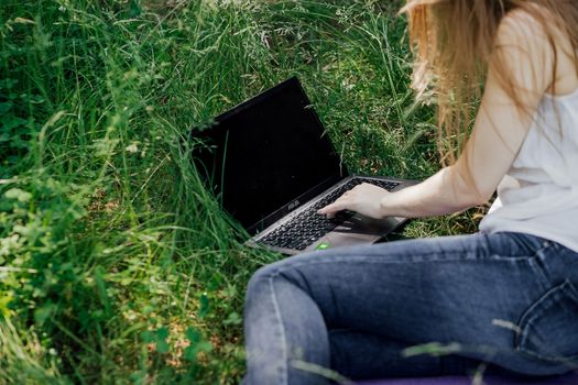 girl sits on the grass and works at a laptop. freelance. selfeducation. the concept of distance learning outdoors