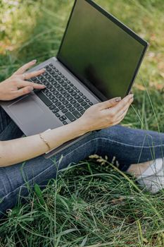 the girl sits on the grass and uses a laptop. Education, lifestyle, technology concept, outdoor learning concept.