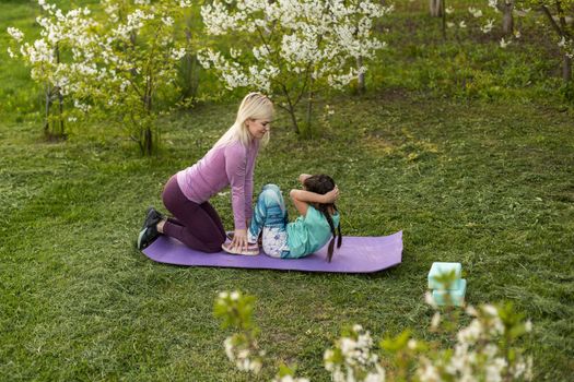 Family Mother teacher training yoga child daughter on a yoga mat at home garden. Family outdoors. Parent with child spends time together. exercise at home concept and new normal