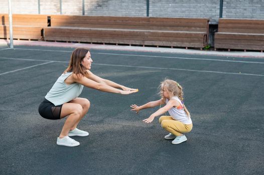 Mother and daughter go in for sports outdoors. Caucasian woman and little girl are engaged in fitness at the stadium