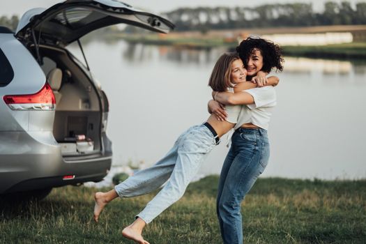 Happy Mother's Day, Woman Hugging with Cheerful Teenage Daughter Outdoors on the Background of Car and Lake