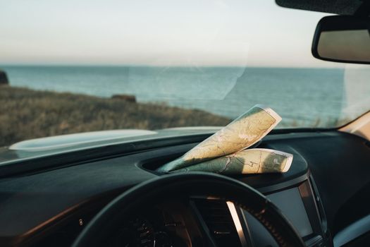 Paper Map Laying on the Dashboard of Car on Background of Sea