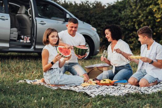 Happy Four Members Family Having Picnic at Sunset, Cheerful Mother and Father with Two Teenage Children Enjoying Weekend Road Trip by Minivan Car