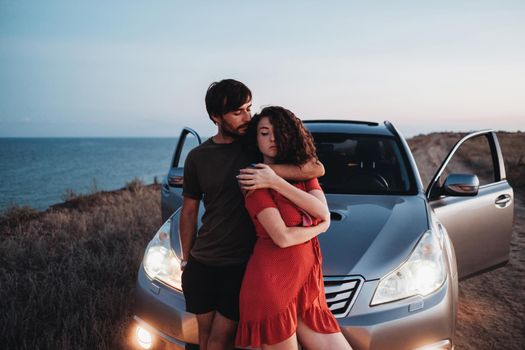 Young Couple Man and Woman Hugging Near Their SUV Car on Seaside After Sunset, Lovers Enjoying Moment Together