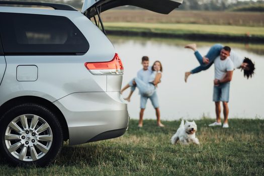 TERNOPIL, Ukraine - September 12 2021: Grey Toyota Sienna with Opened Trunk and Blurred Happy Four Members Family with Pet Dog Having Fun Time Outdoors by River