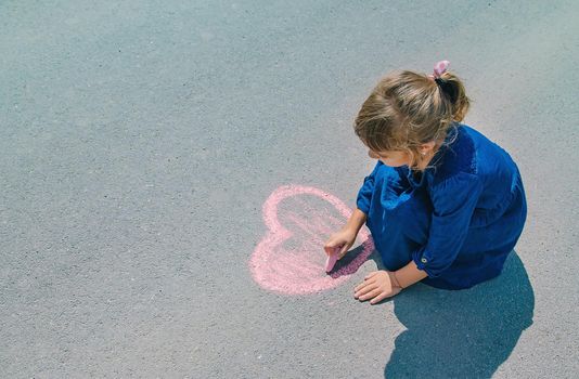 child draws with chalk on the pavement. Selective focus.