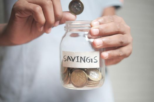 young man hand hold saving coins jar .