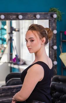 A girl in front of a large mirror in profile with a new make-up and hairstyle. A new look for a young woman. Business concept - beauty salon, facial skin and hair care.