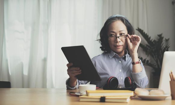 Smiling beautiful senior asian woman using digital tablet at home. work from home concept..