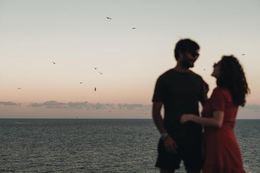 Unfocused Blurred Couple Standing on Background of Sea After Sunset at Evening, Seagulls Flying Over Water