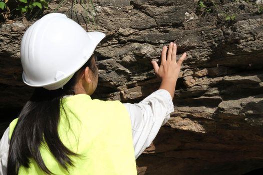 Asian female geologist researcher touches rocks with her hands to analyze surfaces in a natural park. Exploration Geologist in the Field. Stone and ecology concept.