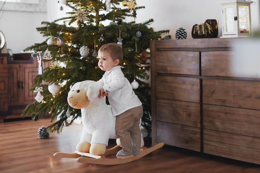 Boy rides a sheep near the Christmas tree at home