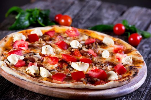 Delicious fresh Pizza with mozzarella, tomatoes, mushrooms, peppers and onion on the wooden background. Top view.