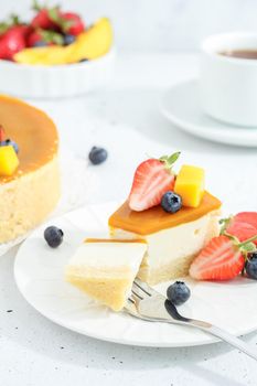 A piece of cheesecake with mango on a plate with a tea fork decorated with berries and flowers on a gray background. Healthy food.