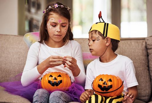 Cropped shot of a young brother and sister eating their Halloween candy while sitting on their sofa at home.