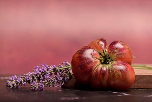 Tiger tomato on a cutting board with basil leaves on wooden background. Copy space. Fresh tomato wased for cooking. Tomato with droplets of water