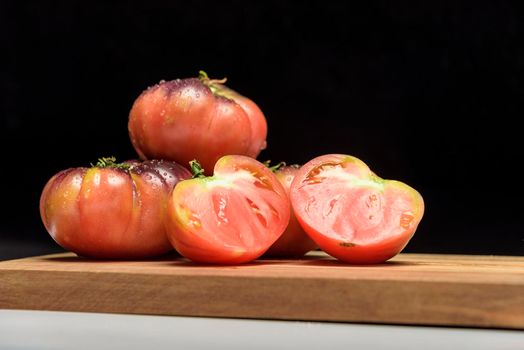 Tiger tomato on a cutting board with basil leaves on wooden background. Copy space. Fresh tomato wased for cooking. Tomato with droplets of water