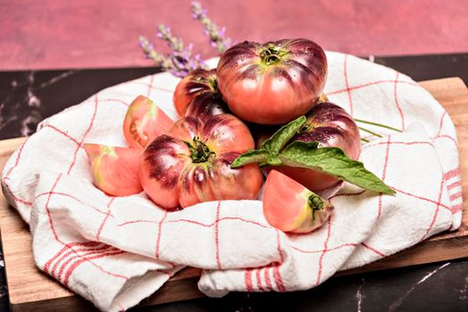 Tiger tomato on a cutting board with basil leaves on wooden background. Copy space. Fresh tomato wased for cooking. Tomato with droplets of water