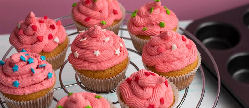 the muffin is on a saucer, decorated with cream and decor. kitchen utensils are in the background. The pink cream is applied in a spiral. Beautiful sweet dessert.