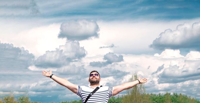 man raised his hands up against the background of the sky with clouds. Smiling, happy. The concept of gratitude and success. Place for text. High quality photo