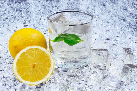 A glass of refreshing ice cold water with a lemon. On the ice background.