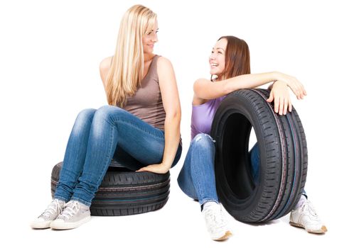 Two young girls sitting on the car wheels, isolated on white.