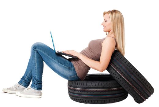 Young sexy woman with laptop sitting on the car wheels, isolated on white