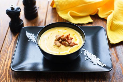 Pumpkin vegetable cream soup on black bowl with pork or chicken meat. Wooden background