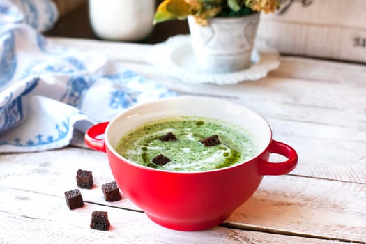 Spinach soup with croutons in red bowl on wooden table