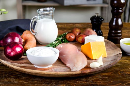 Chicken breasts with fresh healthy vegetables, cheese, oil and spices. Raw products on the wooden background - Stock image