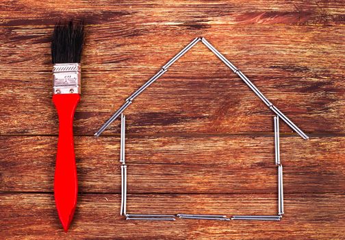 This is an overhead photo of nails in the shape of a home building and brush. There is a lot of space for copy inside the house shape.