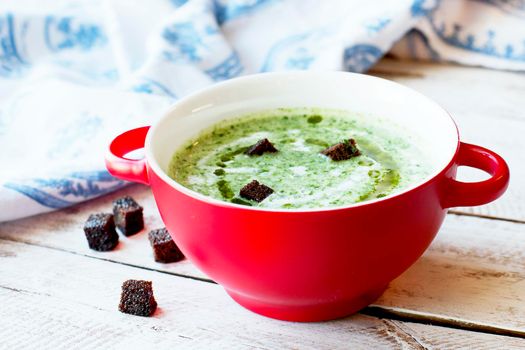 Spinach soup with croutons in red bowl on wooden table