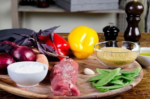 Pork tenderloin with fresh healthy vegetables, oil and spices. Raw products on the wooden background - Stock image