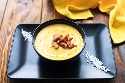 Pumpkin vegetable cream soup on black bowl with pork or chicken meat. Wooden background