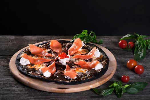 Black pizza with red fish salmon and cream cheese . Base with cuttlefish ink.