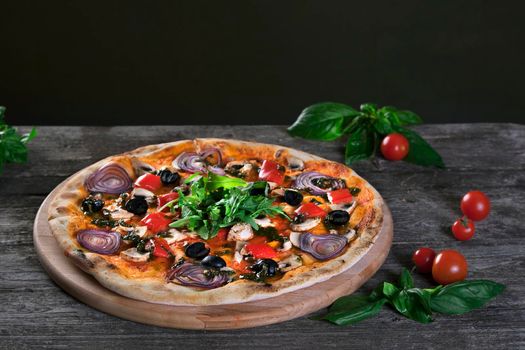 Delicious fresh pizza with onions , black olives , peppers , mushrooms and arugula on the wooden background. Top view.