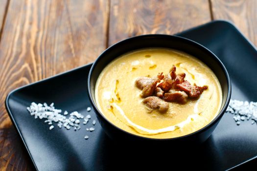 Pumpkin vegetable cream soup on black bowl with pork or chicken meat. Wooden background