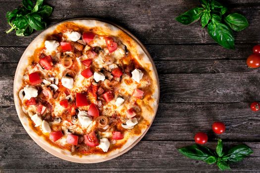 Delicious fresh Pizza with mozzarella, tomatoes, mushrooms, peppers and onion on the wooden background. Top view.
