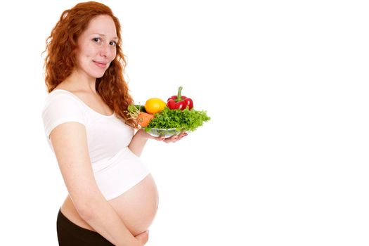 Pregnant woman holding a bowl of vegetables and smiling. Isolated on white.