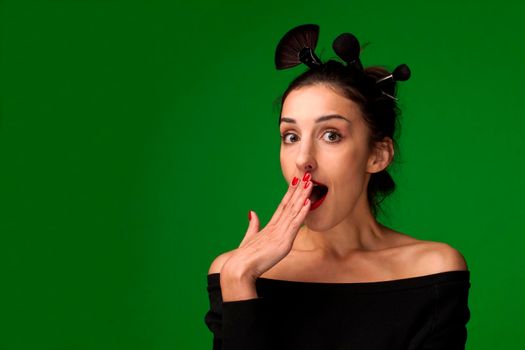 Beautiful surprised woman with makeup brushes in her hair - isolated on green