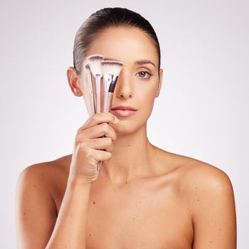 Shot of an attractive young woman holding a set of makeup brushes against a studio background.