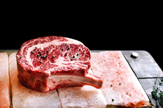 Bone In Rib Eye row Steak on pieces of salt on a wooden board. Stock image