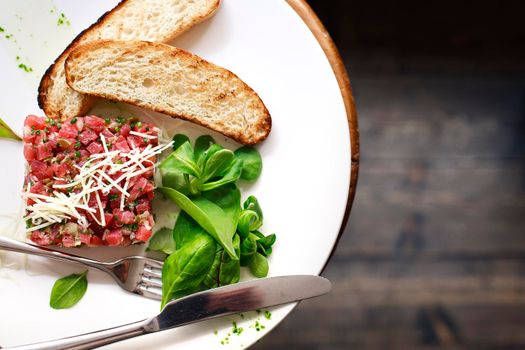 Tartare of beef with spinach on a white plate. Isolated on black or dark wooden background.