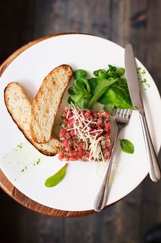 Tartare of beef with spinach on a white plate. Isolated on black or dark wooden background.