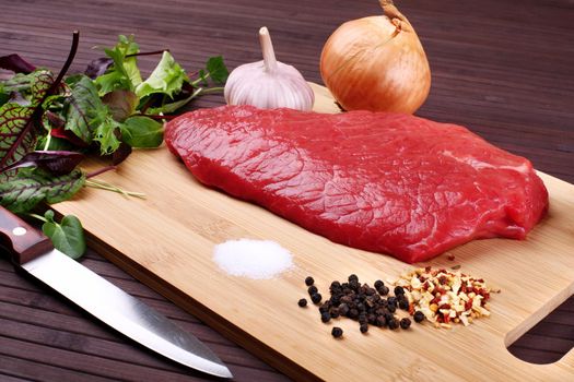 Raw Beef Roast with Fresh Herbs on a dark wooden table.