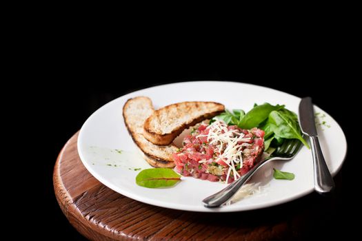 Tartare of beef with spinach on a white plate. Isolated on black.